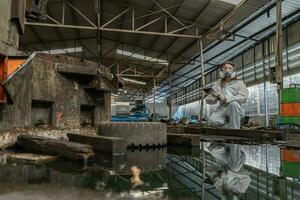 noodgeval verontreiniging fabriek concept. vrouw chemicus vervelend ppe en gas- masker inspecteren olie Aan fabriek verdieping foto