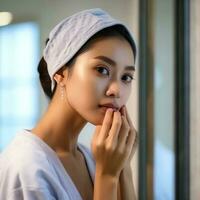 aantrekkelijk versheid Aziatisch vrouw schoon gezicht vers water met zorg kijken naar spiegel in badkamer huis concept door ai gegenereerd foto