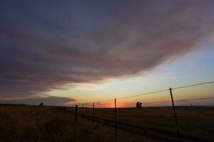 een zonsondergang over- een veld- met een hek en een hek post foto