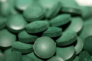 stapel van groen spirulina pillen liet vallen uit van de pot Aan geel achtergrond algen tablets achtergrond top visie dieet supplement alternatief geneeskunde groot grootte super voedsel ogenblik prints voorraad fotografie foto