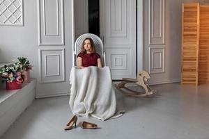 jong meisje, tiener zit in haar kamer op een schommelstoel, bedekt met een deken. rust na een feestje foto
