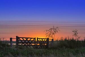 een zonsondergang over- een veld- met een poort foto