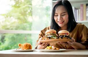 hongerig te zwaar vrouw Holding Hamburger Aan houten bord na levering Mens levert voedingsmiddelen Bij huis. concept van eetbui aan het eten wanorde bed en ontspannende met aan het eten rommel voedsel. foto