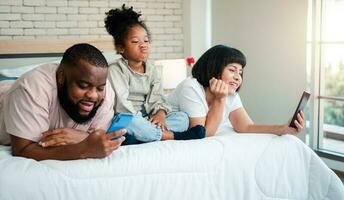 Afro-Amerikaanse meisjes zijn niet tevreden en verdrietig, zittend in het midden tussen vader en moeder. ouders gebruiken de smartphone en verlaten kinderen. kinderen hebben de aandacht van hun ouders nodig. foto