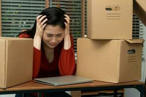 verdrietig Aziatisch vrouw inpakken bezittingen in een karton doos en huilen Aan de bureau in de kantoor na wezen ontslag en werkloos. concept van gevolg Aan de economisch neergang en beheer van de mislukking foto