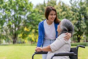 Aziatisch voorzichtig verzorger of verpleegster houden de geduldig hand- en aanmoedigen de geduldig in een rolstoel. concept van gelukkig pensioen met zorg van een verzorger en spaargeld en senior Gezondheid verzekering. foto