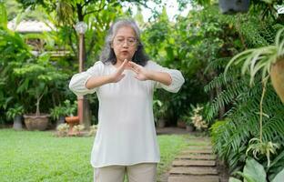portret van een Aziatisch senior vrouw aan het doen yoga en uitrekken oefening in de tuin voor een training. concept van levensstijl geschiktheid en gezond. Aziatisch Dames zijn beoefenen yoga in park. gezond levensstijl foto