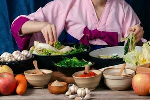 Aziatisch Dames vervelend Koreaans traditioneel kostuums hanbok zijn menging vers roerbak en Kimchi ingrediënten met ingrediënten zo net zo zout, knoflook, gochugaru, vers groenten. foto