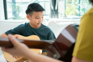 aziatische jongen die gitaar speelt met vader in de woonkamer om hem zoon gitaar te leren spelen, zich gewaardeerd en aangemoedigd te voelen. concept van een gelukkig gezin, leren en leuke levensstijl, liefdesfamiliebanden foto