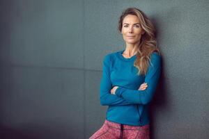 lang haar- mooi midden- oud vrouw slijtage blauw sport- slijtage staand vol vertrouwen Aan de beton muur ai gegenereerd foto