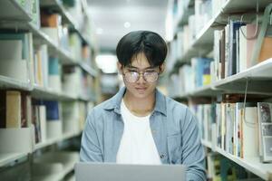 jong Universiteit leerling gebruik makend van laptop voor online aan het leren, zoeken en aan het leren Bij bibliotheek. foto