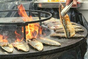 gegrild vis Aan een komvormig vlak rooster met brand gat in de centrum. buitenshuis zeevruchten barbecue Koken. picknick Aan achtertuin Aan Open lucht. straat voedsel concept. voorbereidingen treffen vis over- Open kampvuur foto