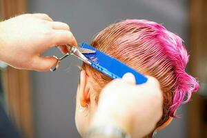 professioneel haar stylist is snijdend kort roze haar- met schaar in haar- salon dichtbij omhoog. foto