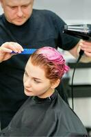 een kapper is drogen de roze haar- van de jong vrouw in een schoonheid salon. foto