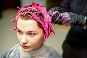 de professioneel kapper toepassingen een borstel naar van toepassing zijn de roze kleurstof naar de haar. haar- kleur concept. foto