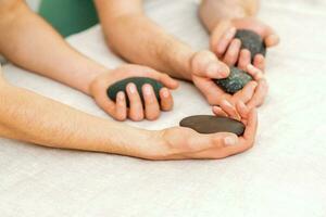 vier handen van mannetje masseurs Holding spa stenen Aan wit handdoek top visie. steen massage concept. foto