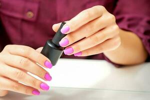 wit vrouw Holding nagel Pools zwart fles met geschilderd roze nagels dichtbij omhoog. foto