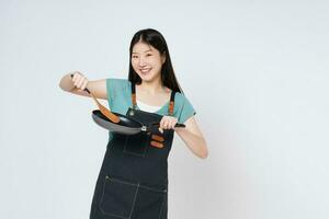 jong vrouw vervelend keuken schort Koken en Holding pan en spatel geïsoleerd Aan wit achtergrond. foto