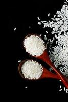wit lang rijst- in houten lepels Aan zwart achtergrond. rauw ongekookt rijst- granen verrijkt met vitamines. foto