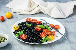 klaar naar eten zwart spaghetti met droog tomaten, sesam zaden en pompoen Aan een bord Aan de tafel. fijnproever voedsel foto