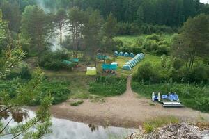 dakspanten tent kamp Aan de rivier- bank. tenten staan in een groen opruimen tegen de achtergrond van de Woud. foto