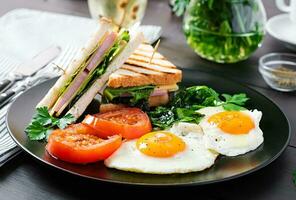 ontbijt. gebakken ei, spinazie, tomaten en club belegd broodje Aan bord. foto