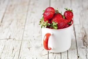 biologische rode aardbeien in witte keramische beker op rustieke houten achtergrond. gezond zoet eten, vitamines en fruitig concept. foto