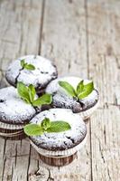 verse chocolade donkere muffins met suikerpoeder en muntblad op rustieke houten tafel. foto