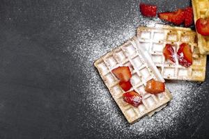 belgische wafels met aardbeien en suikerpoeder op zwarte bordachtergrond. foto