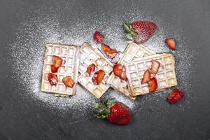 belgische wafels met aardbeien en suikerpoeder op zwarte bordachtergrond. foto