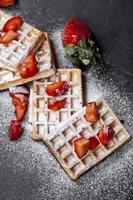 belgische wafels met aardbeien en suikerpoeder op zwart bord. foto