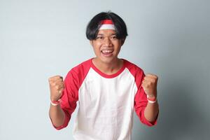 portret van aantrekkelijk Aziatisch Mens in t-shirt met rood en wit lint Aan hoofd, verhogen zijn vuist, vieren Indonesië's onafhankelijkheid dag. geïsoleerd beeld Aan grijs achtergrond foto