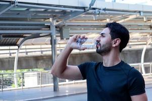 knappe mannen in sportkleding drinkwater uit plastic flessen na het sporten in de buitenlucht foto