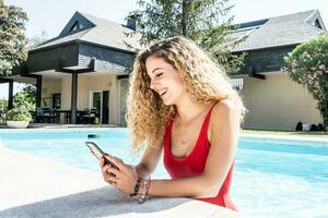 vrouw in een rood zwempak binnen een zwembad gebruik makend van haar cel telefoon foto