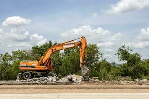 een visie van een geel backhoe geparkeerd Aan de bestrating van een afgebroken beton weg. foto