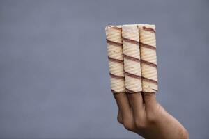 hand vasthouden wafel broodjes met chocola Aan grijs achtergrond, dichtbij omhoog foto