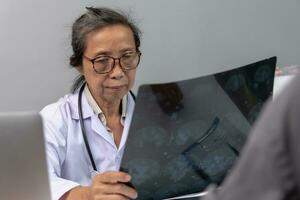 Aziatisch vrouw dokter aan het kijken geduldig röntgenstraal film, mri en ct scannen. Gezondheid zorg concept. foto