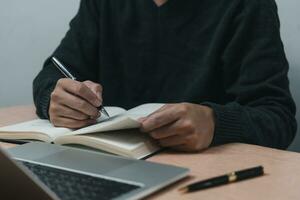 Mens handen met pen schrijven Aan notitieboekje in de kantoor.leren, onderwijs en werk.schrijft doelen, plannen, maken naar Doen en wens lijst Aan bureau. foto