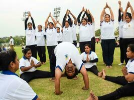 nieuw Delhi, Indië, juni 21, 2023 - groep yoga oefening sessie voor mensen Bij Yamuna sport- complex in Delhi Aan Internationale yoga dag, groot groep van volwassenen Bijwonen yoga klasse in krekel stadion foto