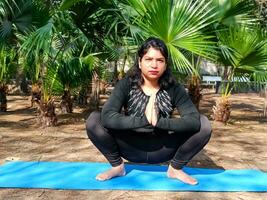 jong Indisch vrouw beoefenen yoga buitenshuis in een park. mooi meisje praktijk eenvoudig yoga houding. rust en kom tot rust, vrouw geluk. eenvoudig yoga poses buitenshuis foto