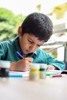 slim Indisch weinig jongen uitvoeren duim schilderij met verschillend kleurrijk water kleur uitrusting gedurende de zomer vakanties, schattig Indisch kind aan het doen kleurrijk duim schilderij tekening Aan houten tafel foto