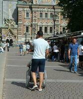 Sankt petersburg Rusland - 08 09 2023 jong Mens verzorger voortvarend rolstoel met vrouw persoon met onbekwaamheid aan de overkant stad straat foto