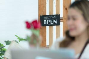 vrouw gebruik makend van laptop met Open teken in bloemen winkel. bedrijf concept. foto