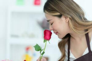 jong vrouw bloemist ruiken een rood roos in de bloem winkel foto