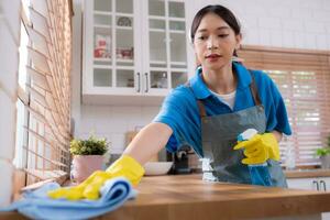 schoonmaak onderhoud. detailopname van vrouw in schort en rubber handschoenen schoonmaak houten tafel met verstuiven foto