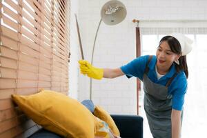 jong Dames schoonmaak hulp in de huishouding in uniform zijn schoonmaak de leven kamer Bij huis. foto