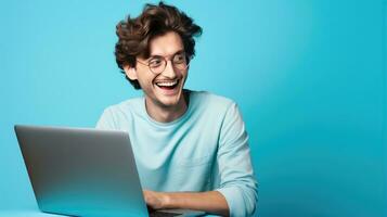 portret van gelukkig freelancer Mens zittend Bij bureau met laptop Aan blauw achtergrond. jong ondernemend vent genieten van afgelegen werk gemaakt met generatief al technologie foto