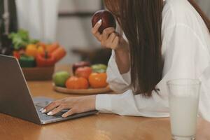 portret van mooi freelancer vrouw werken typen Aan laptop computer zittend Bij tafel glimlachen op zoek naar scherm in keuken. aantrekkelijk roodharige jong vrouw afgelegen werken Aan laptop van huis kantoor. foto