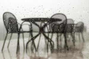 waterdruppels op glazen raam restaurant terras uitzicht door raam met regendruppels op regenachtige dag slecht weer behang foto