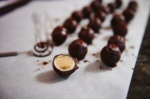 chocola truffels Aan perkament papier en accent in de voorgrond met chocolaatjes besnoeiing in voor de helft en gevuld met gezouten karamel. foto